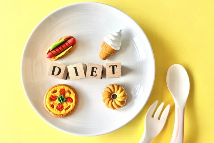ダイエットと書かれた木製のブロックと高カロリーな食べ物のミニチュアを並べた画像